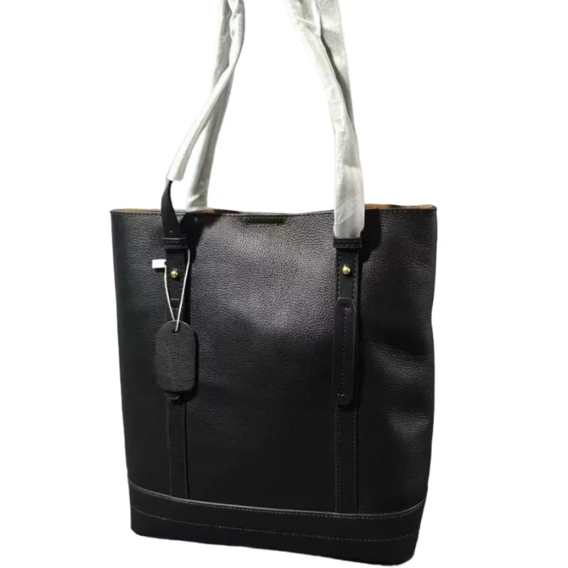 Leather vertical tote bag with riveted wide shoulder strap, decorative leather tag, stitched bottom panels, and large capacity.